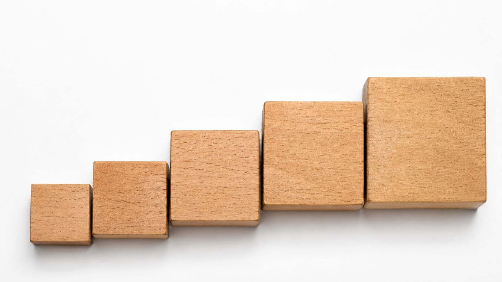 A row of wooden building blocks arranged in increasing sizes, like steps, illustrating incremental growth
