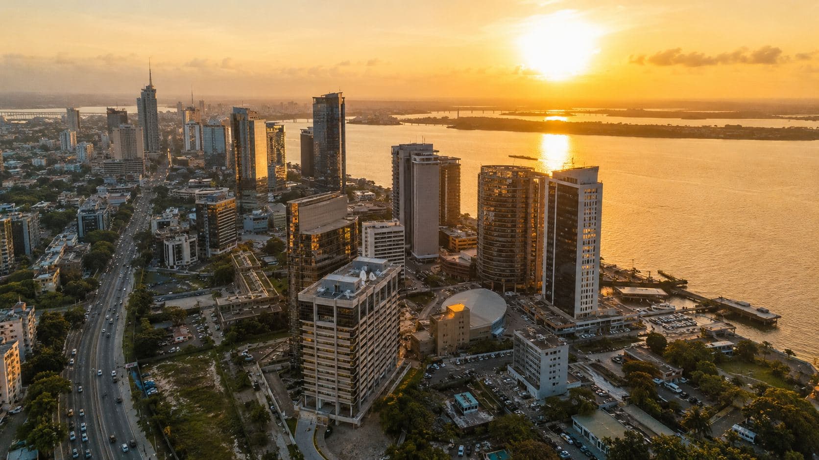 Aerial view of a coastal Nigerian city skyline at sunset, with skyscrapers lining the waterfront